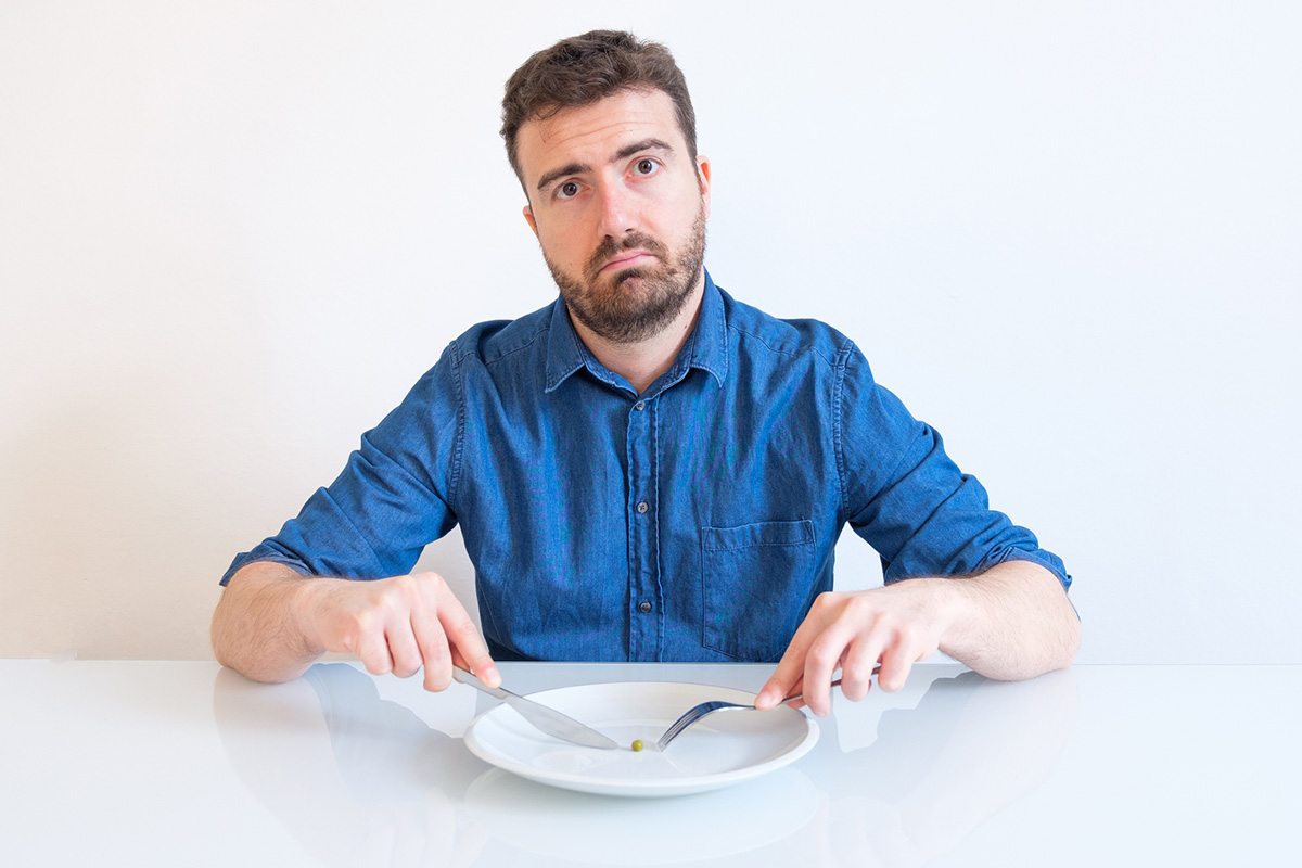 hombre tratando de comer un chícharo con cuchillo y tenedor