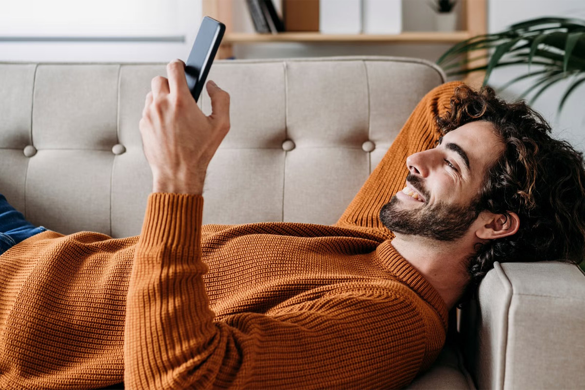 hombre acostado en el sillón viendo su celular