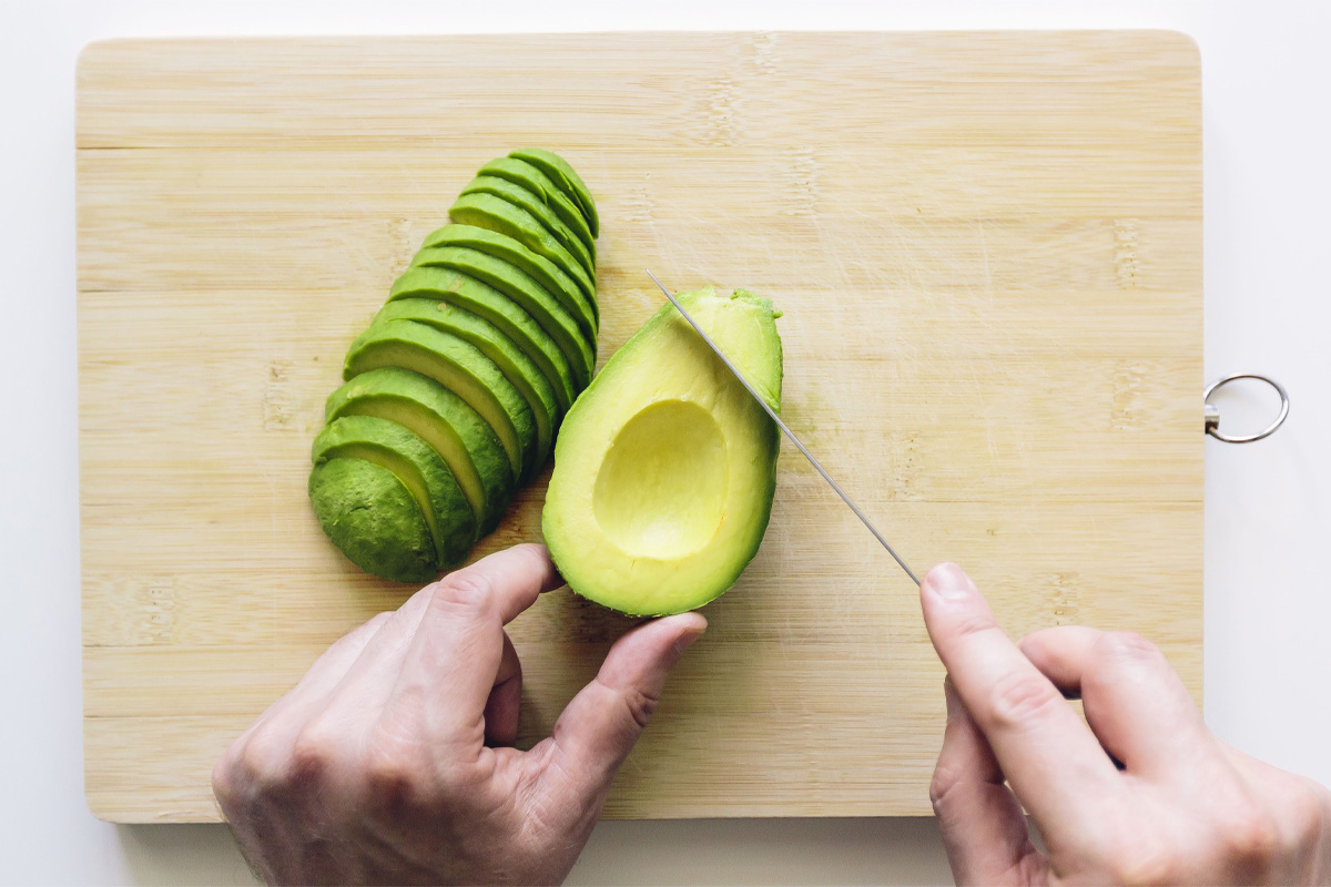 hombre partiendo un aguacate en una tabla para cortar