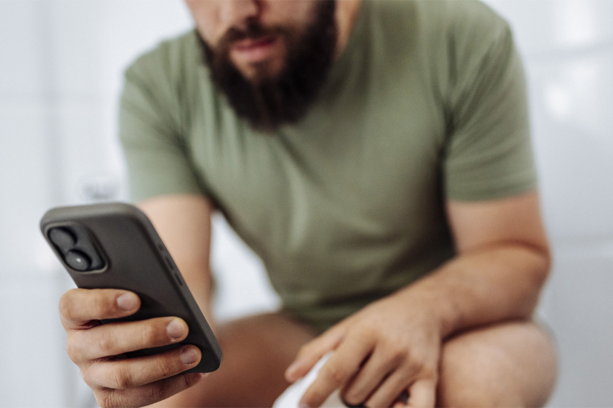hombre revisando el celular mientras está sentado en el baño